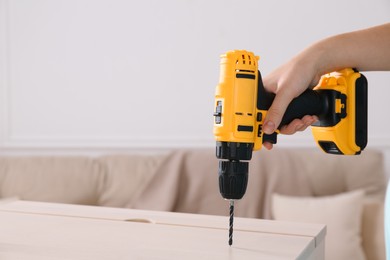 Photo of Woman with electric screwdriver assembling furniture at home, closeup. Space for text