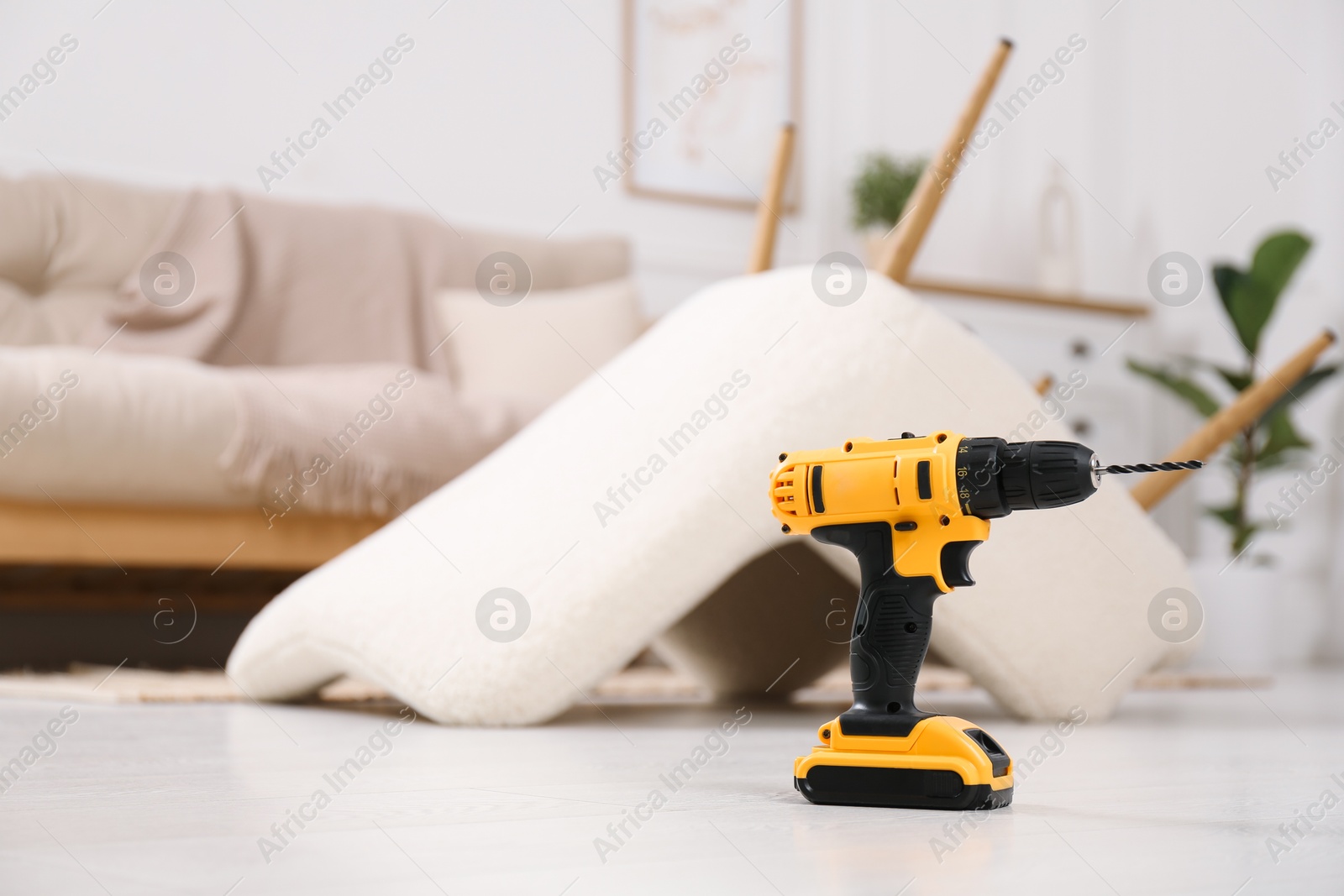 Photo of Cordless electric screwdriver on floor at home. Space for text