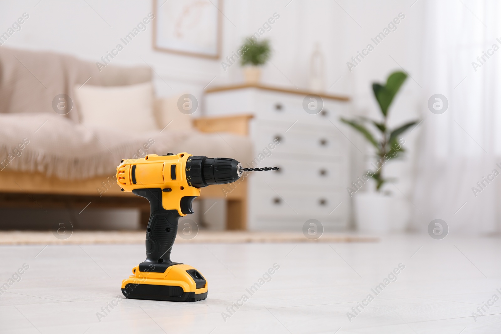 Photo of Cordless electric screwdriver on floor at home. Space for text