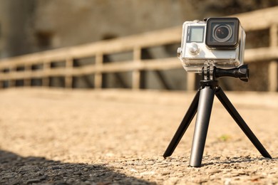 Modern action camera with tripod outdoors. Space for text