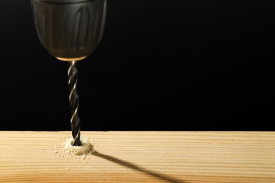 Photo of Drilling hole in wooden plank on black background, closeup. Space for text