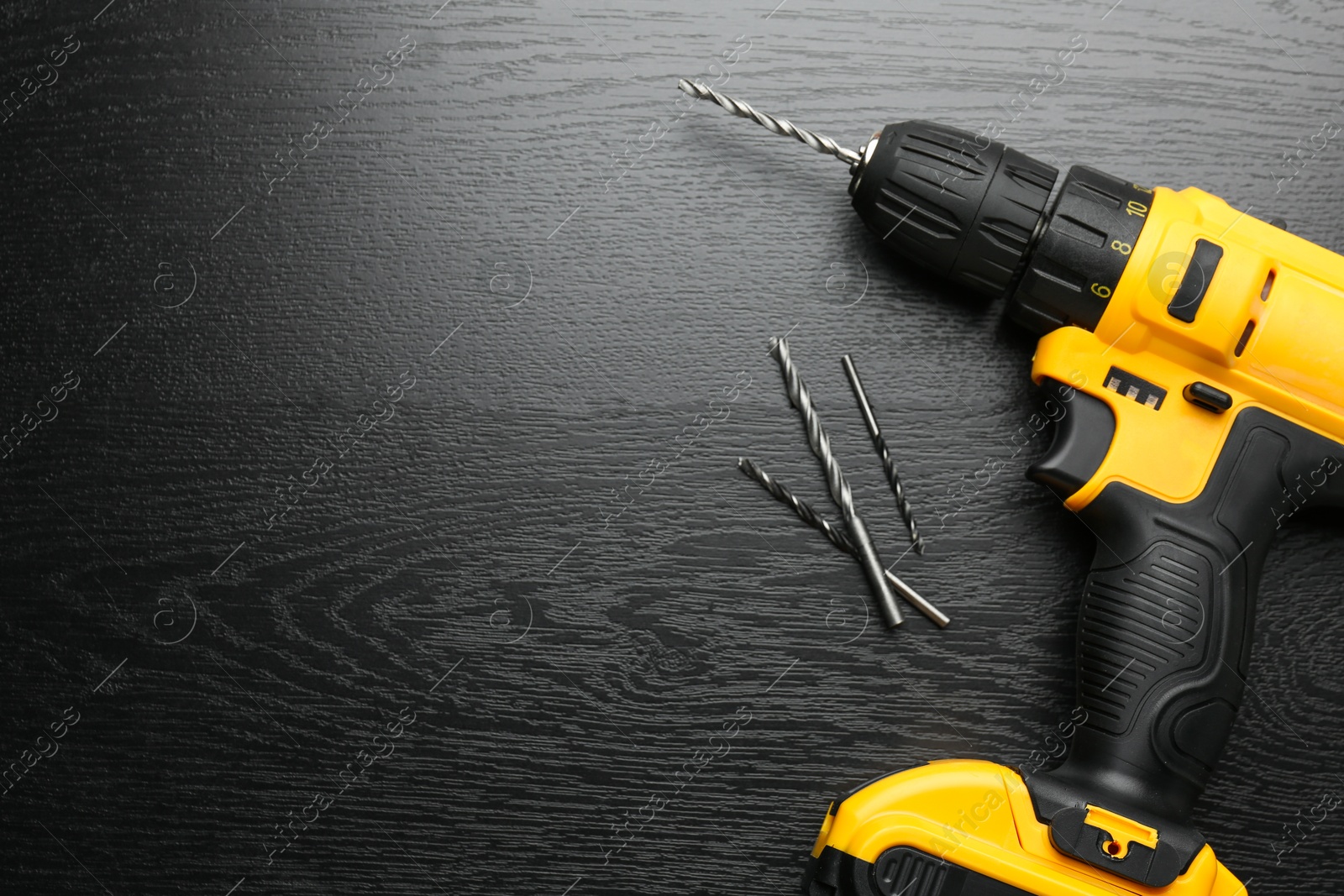 Photo of Cordless electric drill and bits on black wooden table, flat lay. Space for text