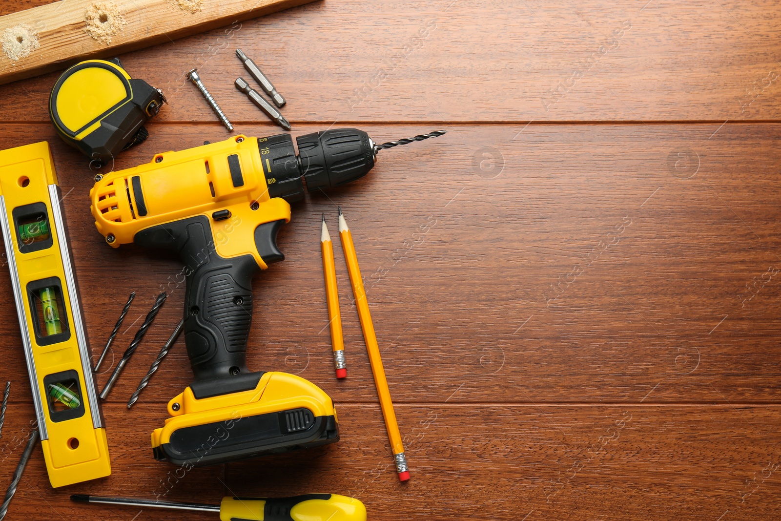 Photo of Cordless electric drill, pencils and construction tools on wooden table, flat lay. Space for text