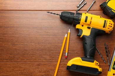 Cordless electric drill, pencils and bits on wooden table, flat lay. Space for text