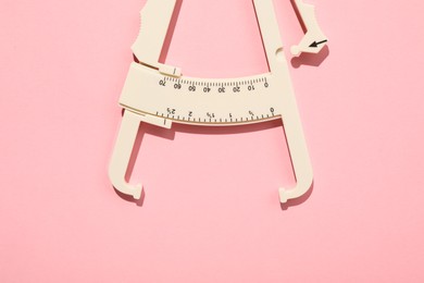 Photo of Plastic body fat caliper on pink background, top view