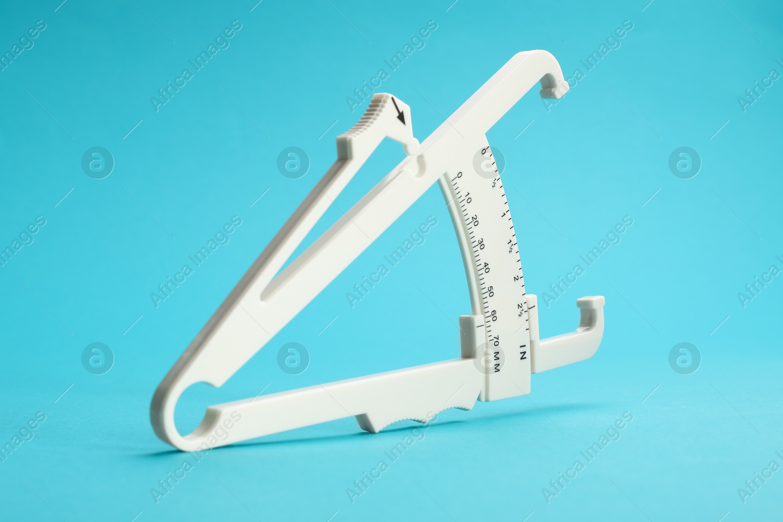 Photo of Plastic body fat caliper on light blue background, closeup