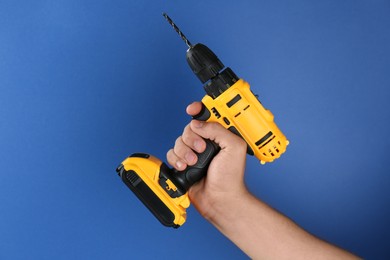 Photo of Man with cordless electric drill on blue background, closeup