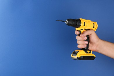 Photo of Man with cordless electric drill on blue background, closeup. Space for text