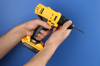 Photo of Man with cordless electric drill on blue background, closeup