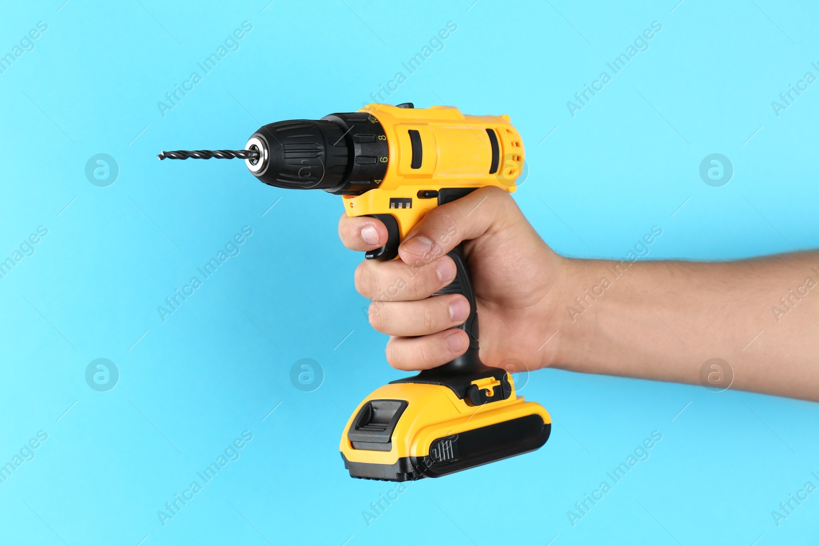 Photo of Man with cordless electric drill on light blue background, closeup