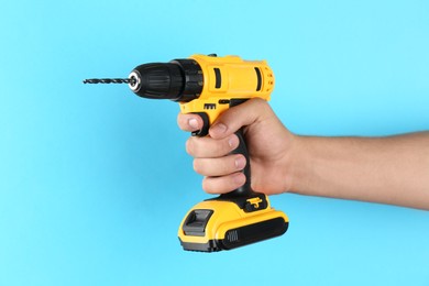 Man with cordless electric drill on light blue background, closeup