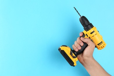 Photo of Man with cordless electric drill on light blue background, closeup. Space for text