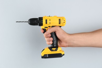 Photo of Man with cordless electric drill on light grey background, closeup