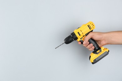 Man with cordless electric drill on light grey background, closeup. Space for text