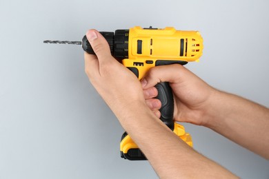 Photo of Man with cordless electric drill on light grey background, closeup