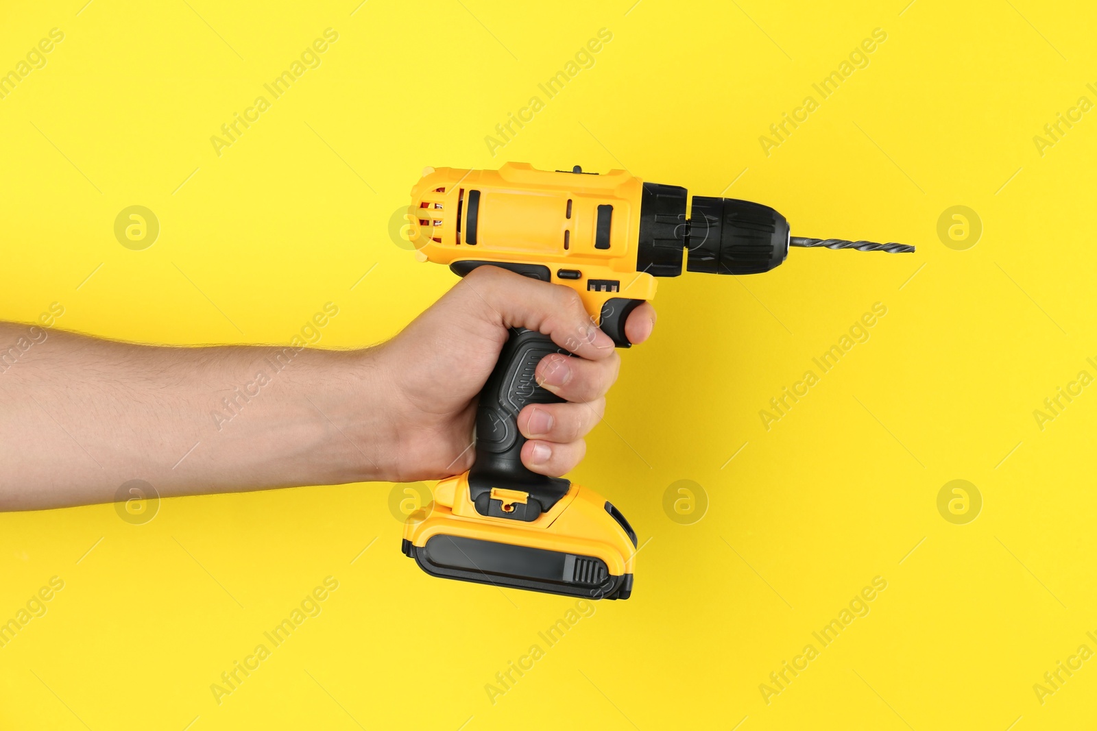 Photo of Man with cordless electric drill on yellow background, closeup