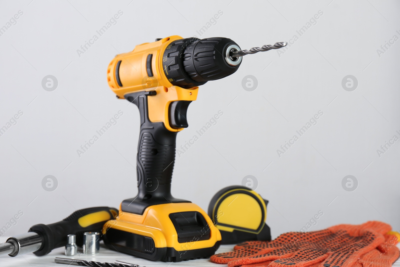 Photo of Cordless electric drill, gloves, bits, screwdriver and measuring tape on table