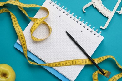 Photo of Flat lay composition with body fat caliper, measuring tape and notebook on light blue background