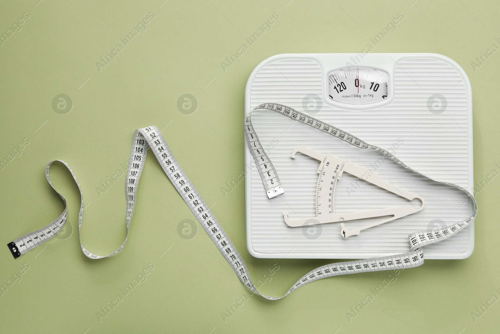 Photo of Body fat caliper, measuring tape and scale on light green background, flat lay