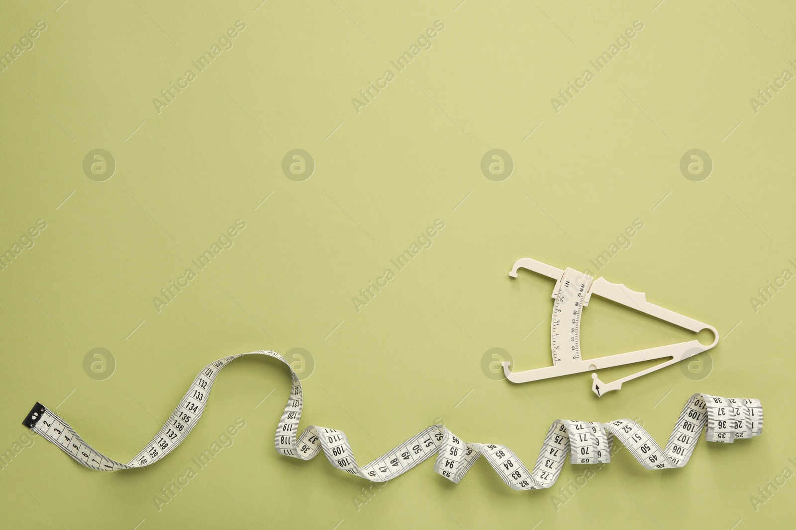 Photo of Body fat caliper and measuring tape on light green background, flat lay. Space for text