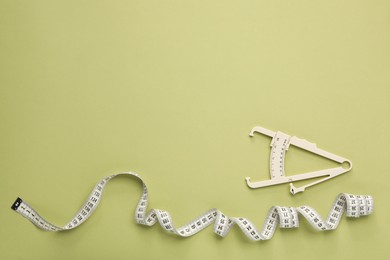 Photo of Body fat caliper and measuring tape on light green background, flat lay. Space for text