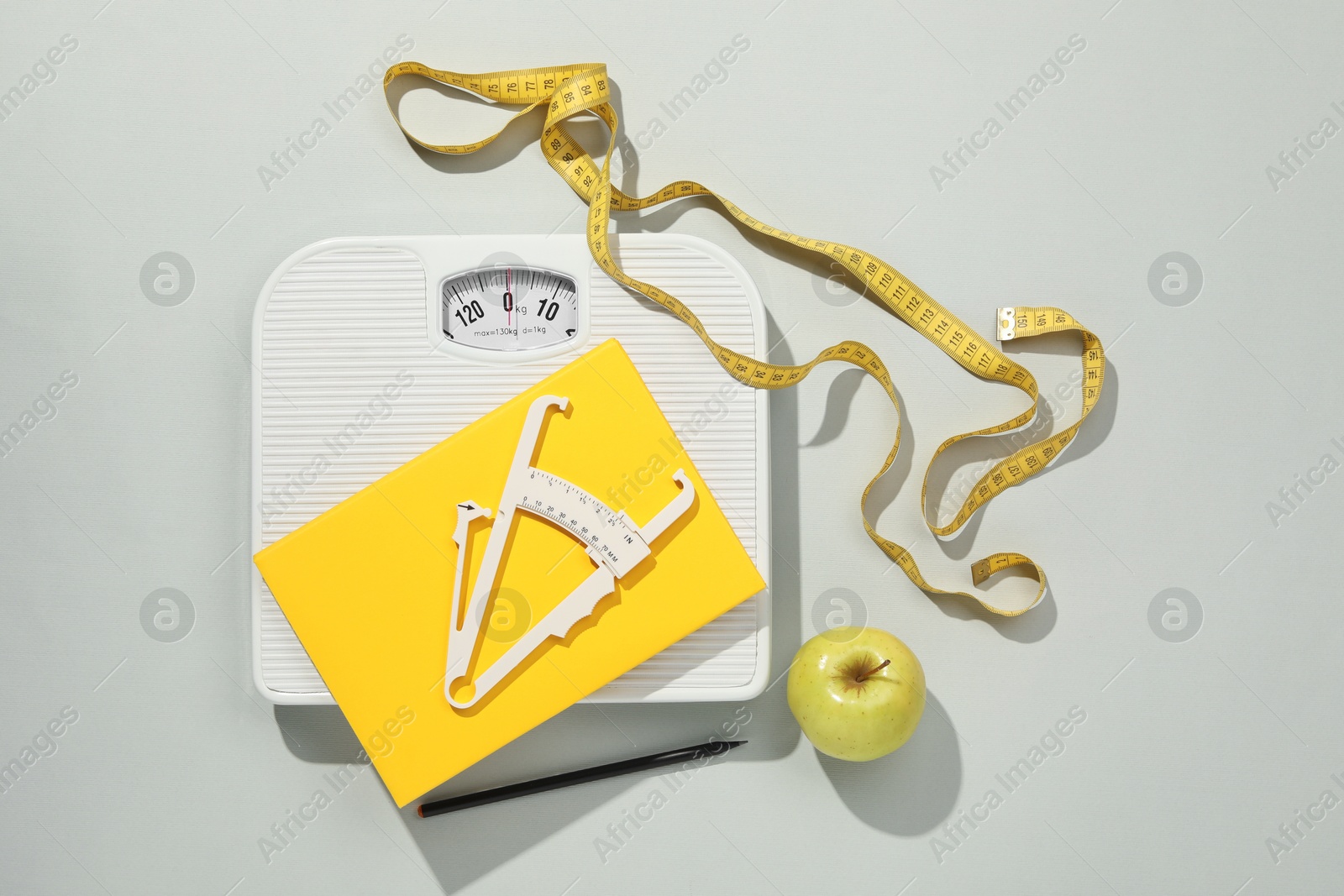 Photo of Body fat caliper, measuring tape, scale and notebook on light grey background, flat lay