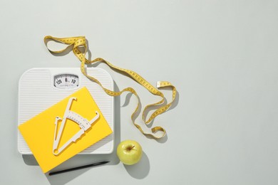 Photo of Body fat caliper, measuring tape, scale and notebook on light grey background, flat lay. Space for text