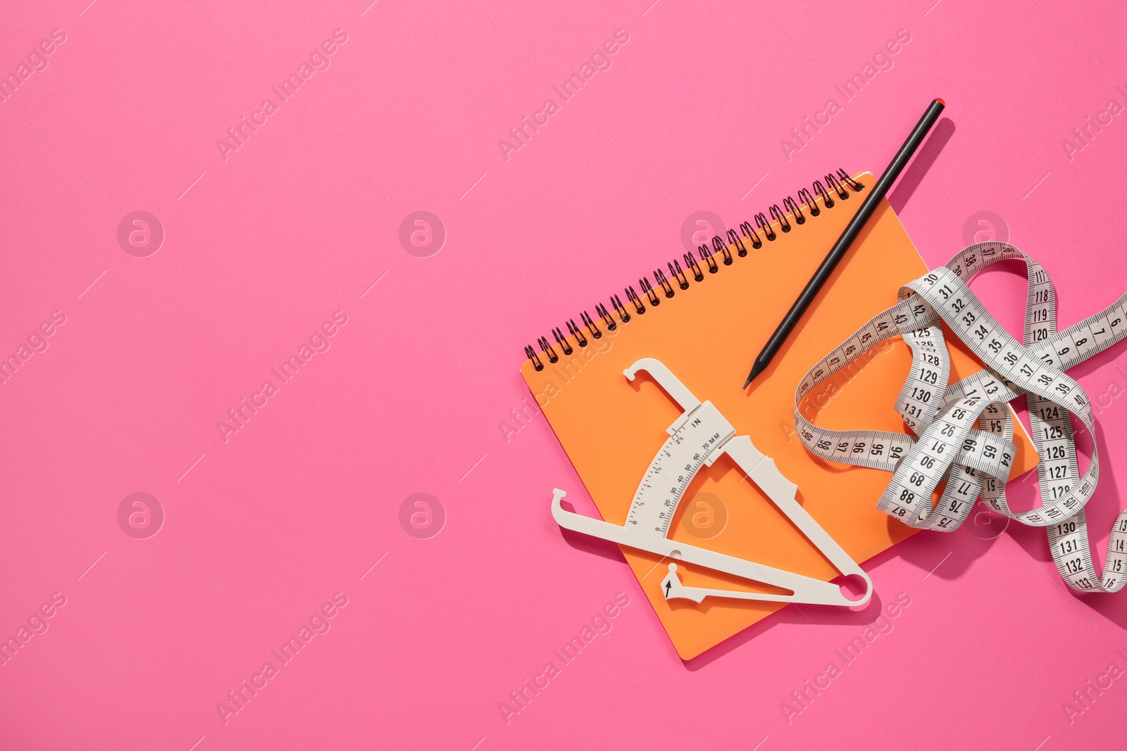 Photo of Body fat caliper, measuring tape, notebook and pencil on pink background, flat lay. Space for text