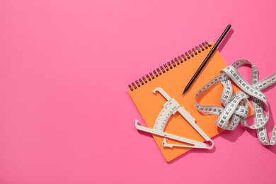 Photo of Body fat caliper, measuring tape, notebook and pencil on pink background, flat lay. Space for text