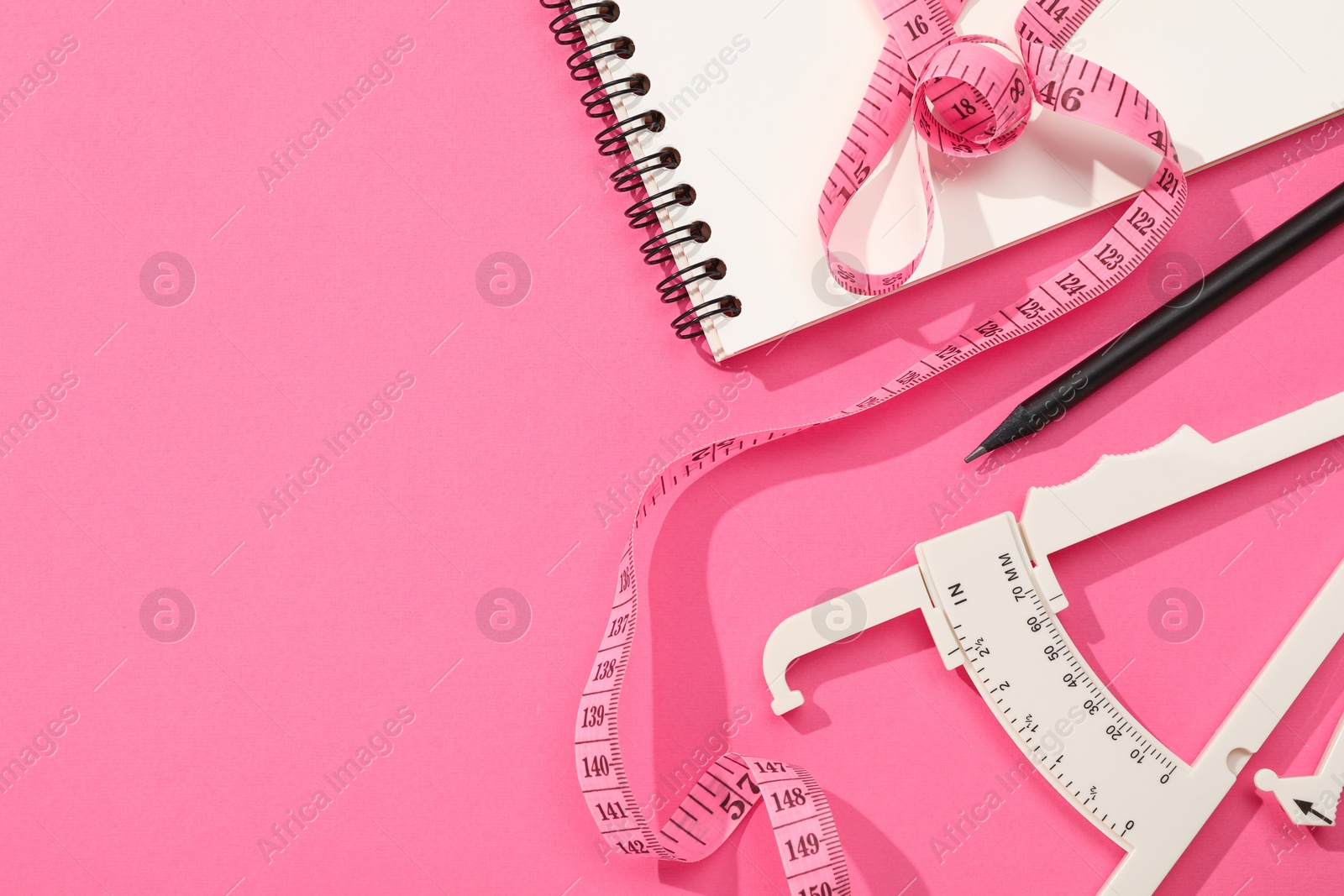 Photo of Body fat caliper, measuring tape, notebook and pencil on pink background, flat lay. Space for text