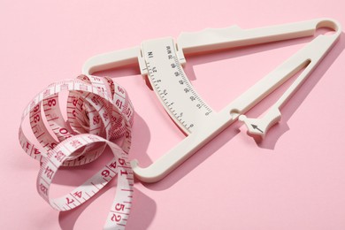 Photo of Body fat caliper and measuring tape on pink background, closeup