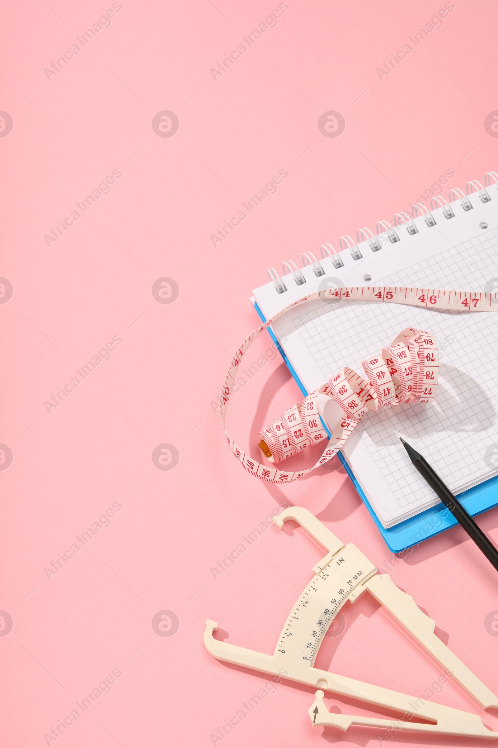 Photo of Body fat caliper, measuring tape, notebook and pencil on pink background. Space for text