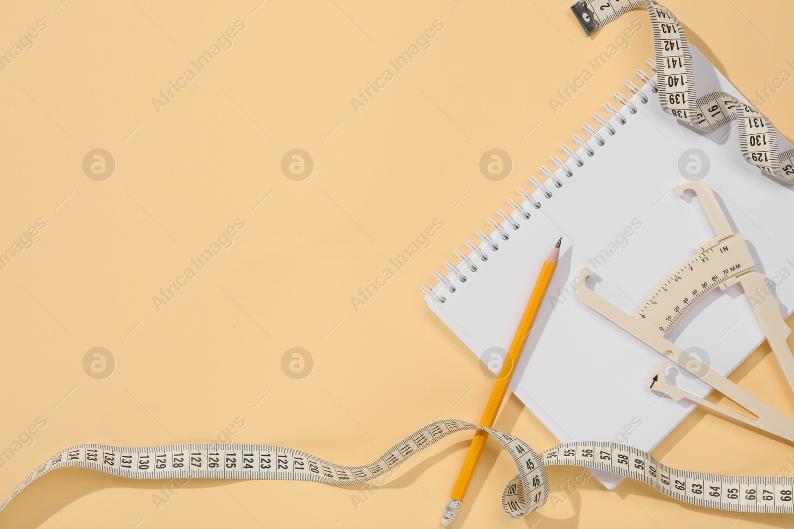 Photo of Body fat caliper, measuring tape, pencil and notebook on beige background, flat lay. Space for text