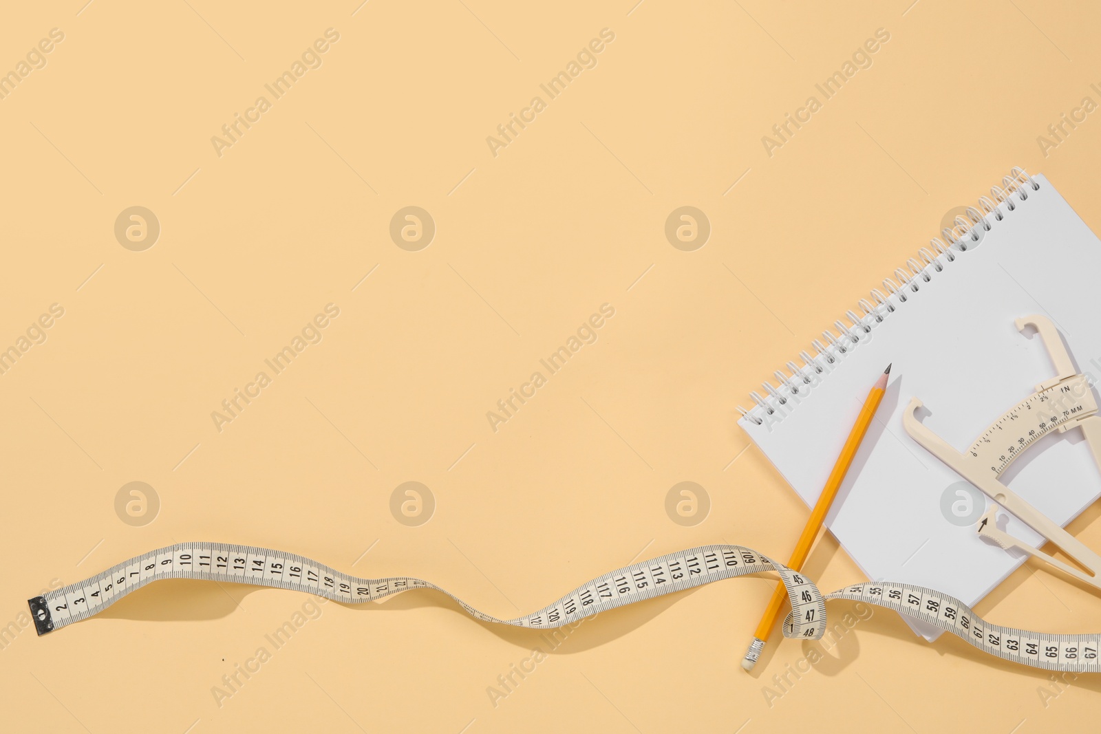 Photo of Body fat caliper, measuring tape, pencil and notebook on beige background, flat lay. Space for text