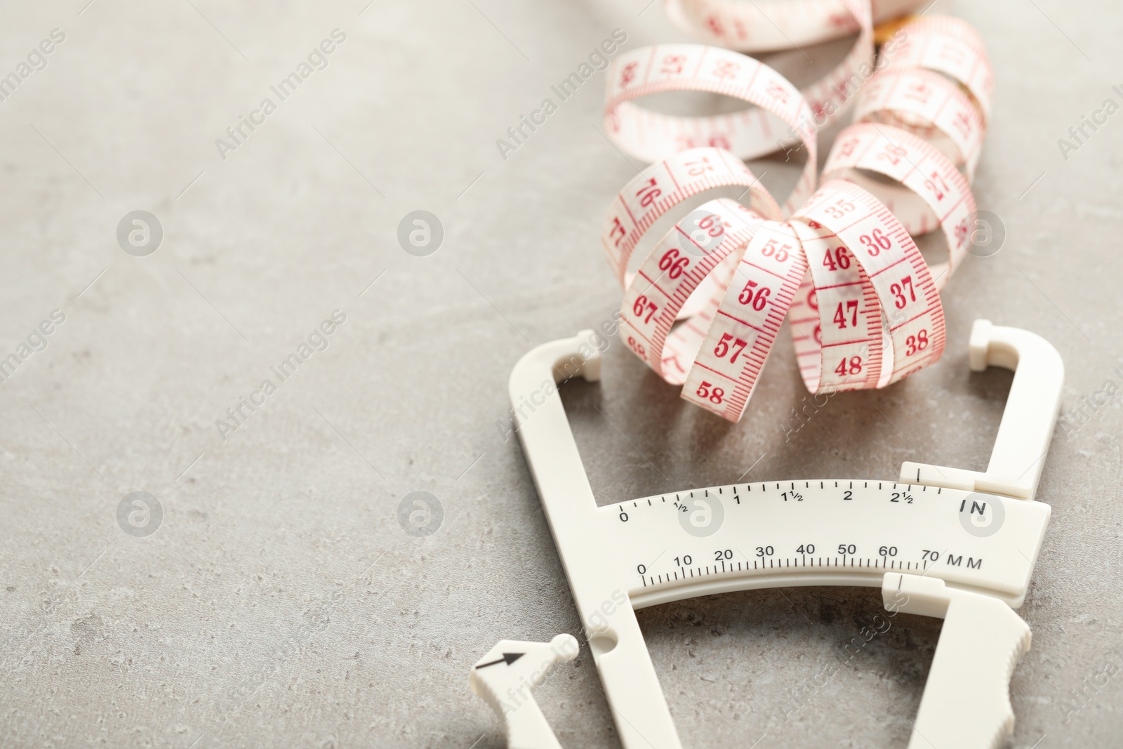 Photo of Plastic body fat caliper and measuring tape on grey table, closeup. Space for text