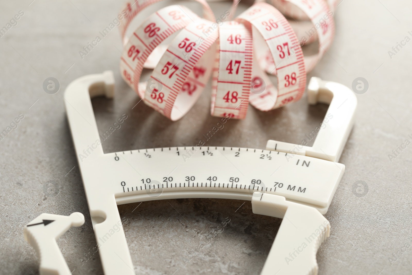 Photo of Plastic body fat caliper and measuring tape on grey table, closeup