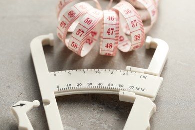 Photo of Plastic body fat caliper and measuring tape on grey table, closeup