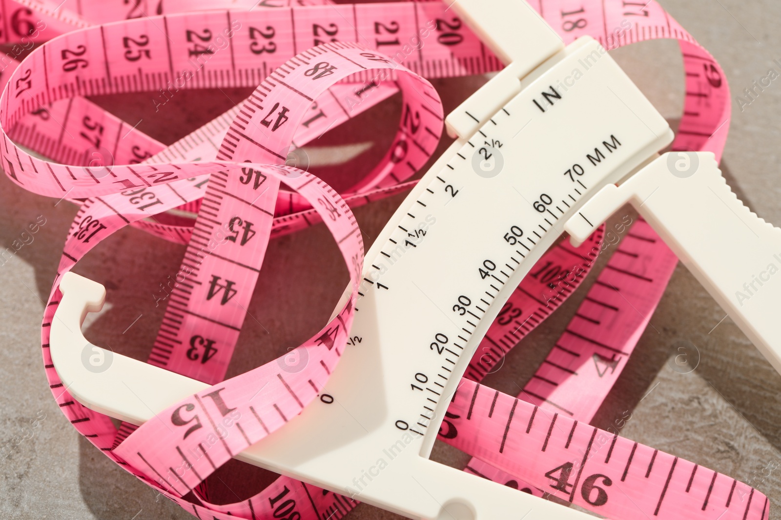 Photo of Plastic body fat caliper and measuring tape on grey table, closeup