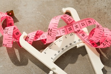 Photo of Plastic body fat caliper and measuring tape on grey table, closeup