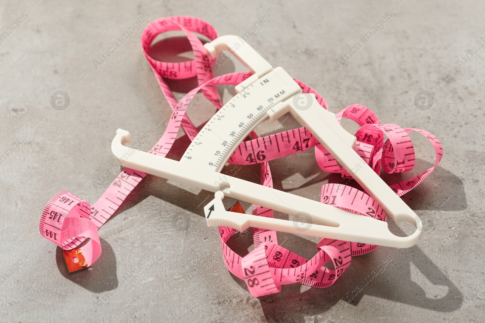 Photo of Plastic body fat caliper and measuring tape on grey table, closeup