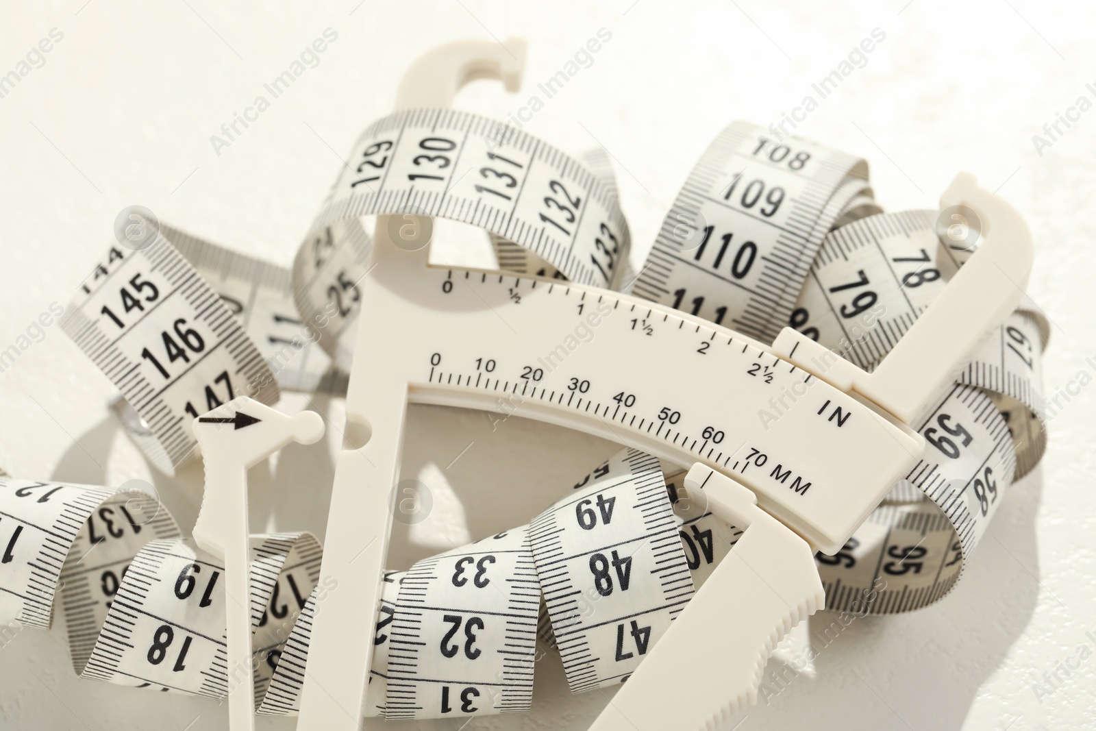 Photo of Plastic body fat caliper and measuring tape on white table, closeup