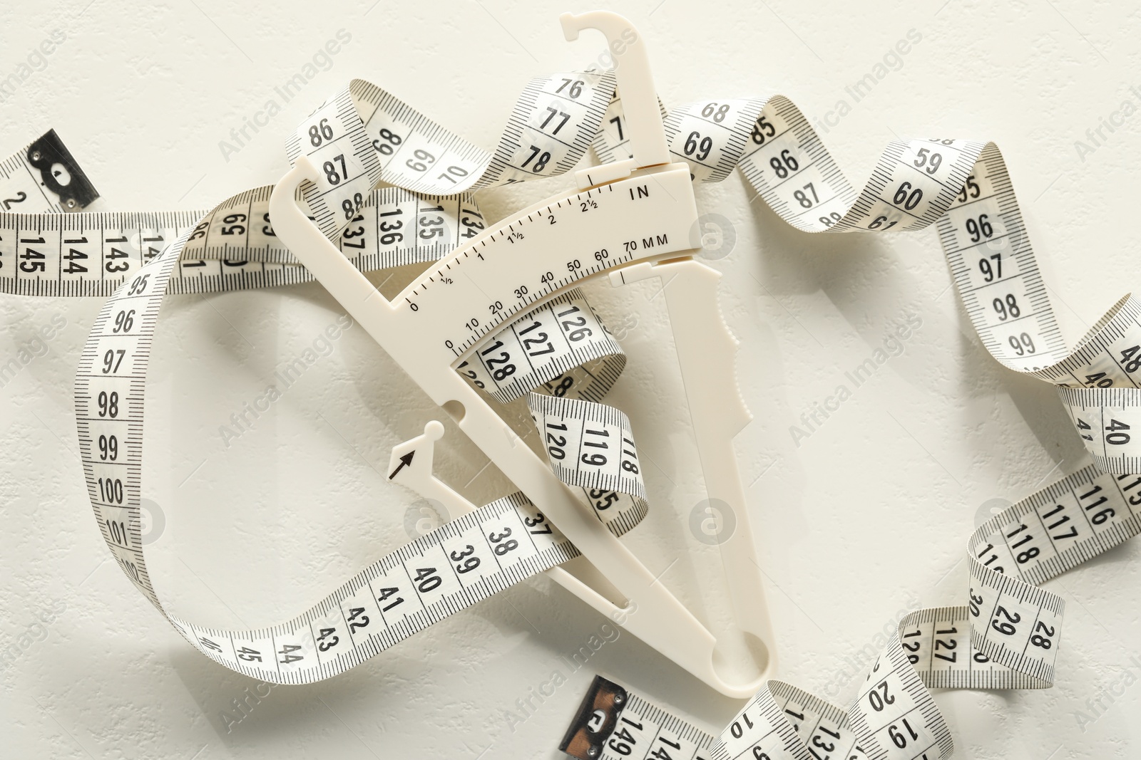 Photo of Plastic body fat caliper and measuring tape on white table, top view