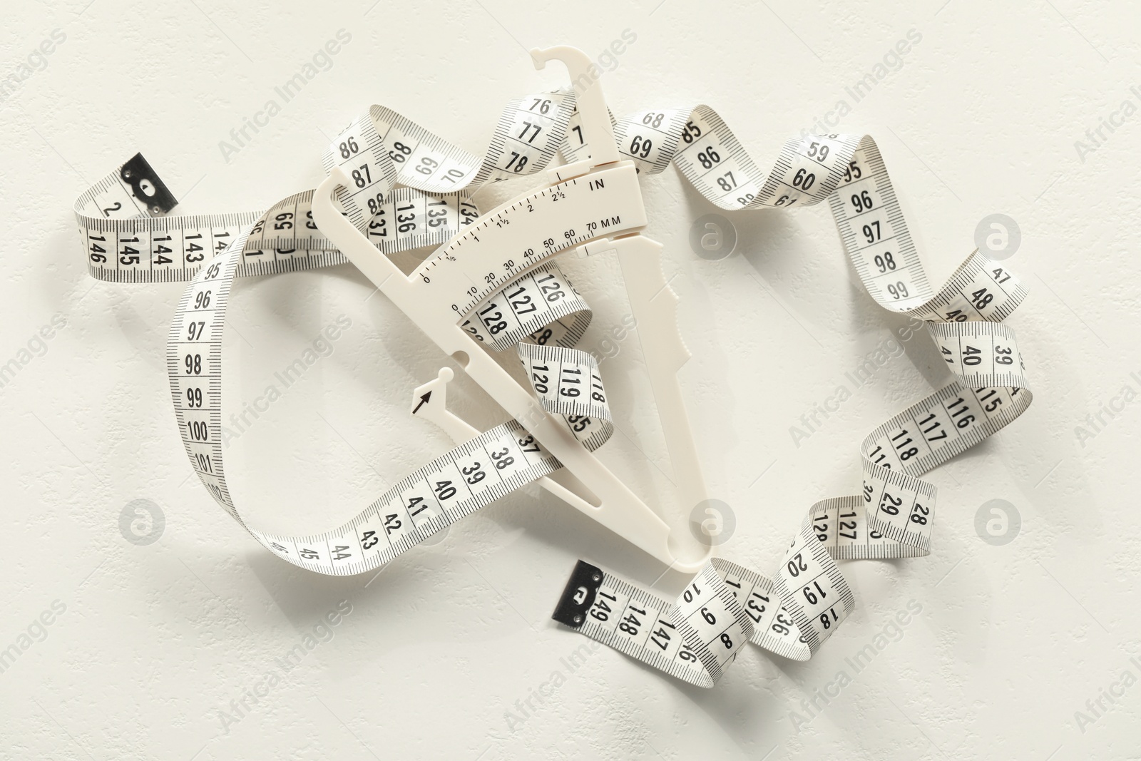 Photo of Plastic body fat caliper and measuring tape on white table, top view