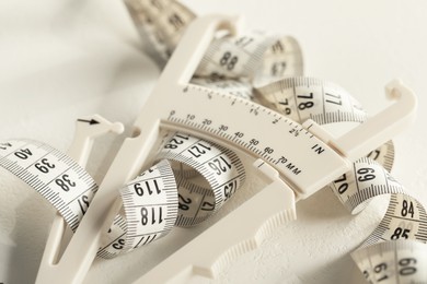 Photo of Plastic body fat caliper and measuring tape on white table, closeup