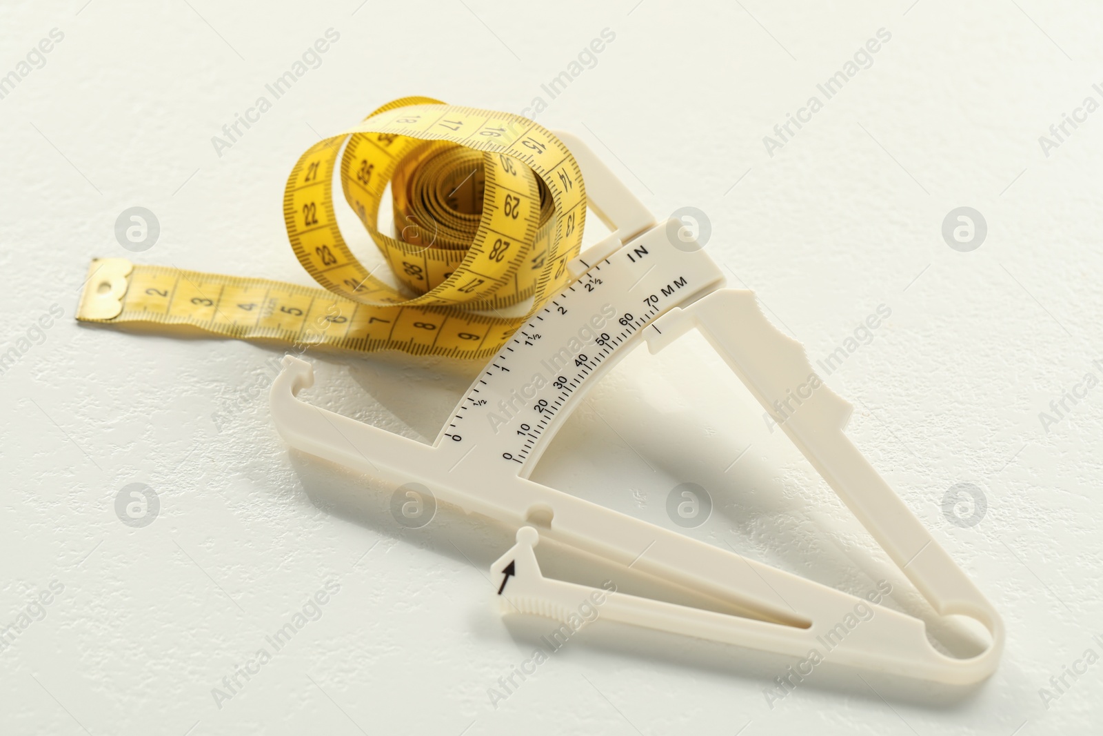 Photo of Plastic body fat caliper and measuring tape on white table, closeup