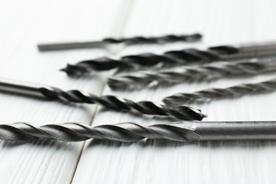 Photo of Many different drill bits on white wooden table, closeup