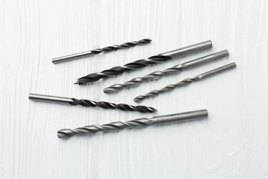 Photo of Many different drill bits on white wooden table, top view