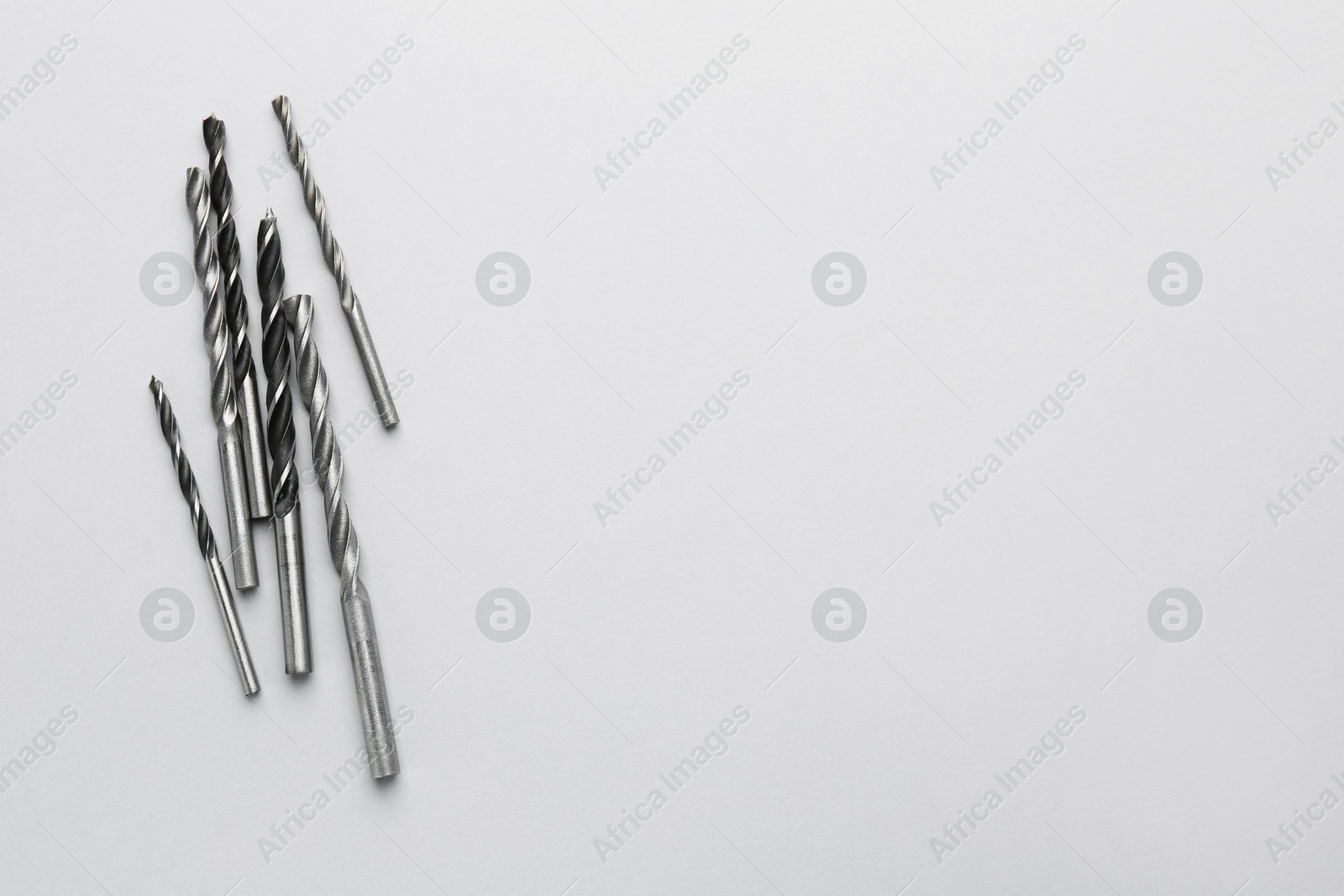 Photo of Many different drill bits on light grey background, top view. Space for text