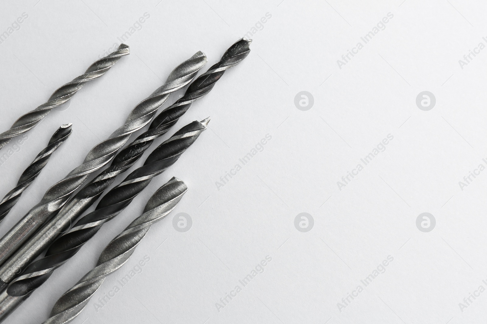 Photo of Many different drill bits on light grey background, top view. Space for text