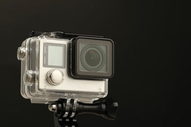 Photo of Modern action camera and mount against black background, closeup. Space for text